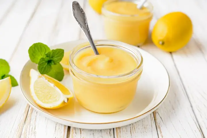 Un pot de crème citron onctueuse, garni de menthe fraîche et de quartiers de citron, prêt à être dégusté.