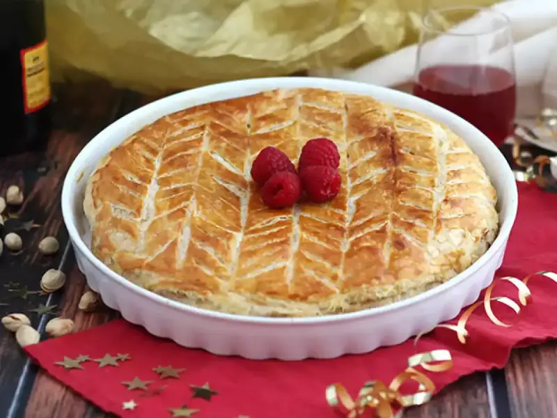 Une délicieuse galette pistache framboise dorée, décorée de fruits rouges frais, prête à être dégustée.